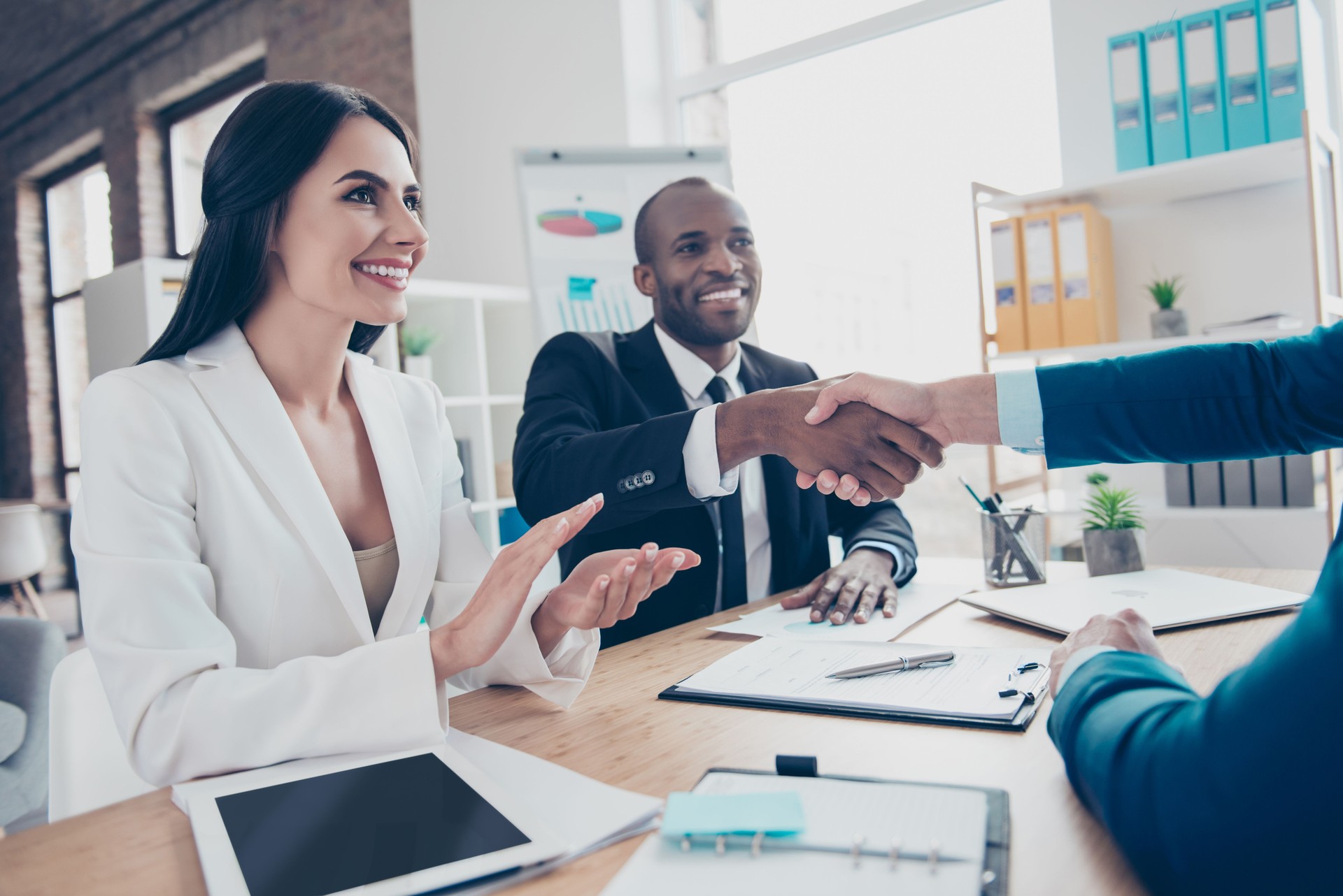 Two successful executive businesspeople celebrate completed  deal about their business with lawyer, sitting in work place, station, wearing suits, men shaking hands, woman applaud to them